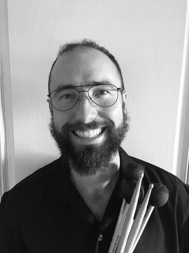 Mark McCafferty black and white profile holding marimba mallets and drumsticks
